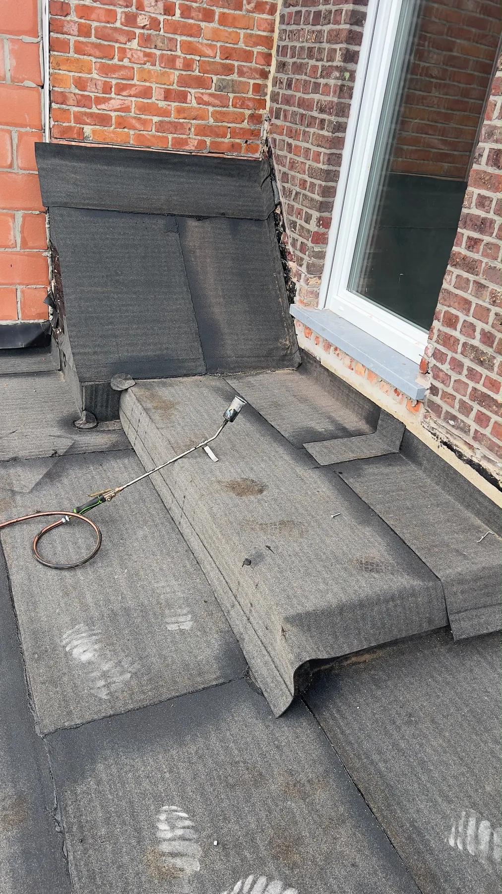 De roofing wordt tegen de gevel en onder het raam omhoog gewerkt